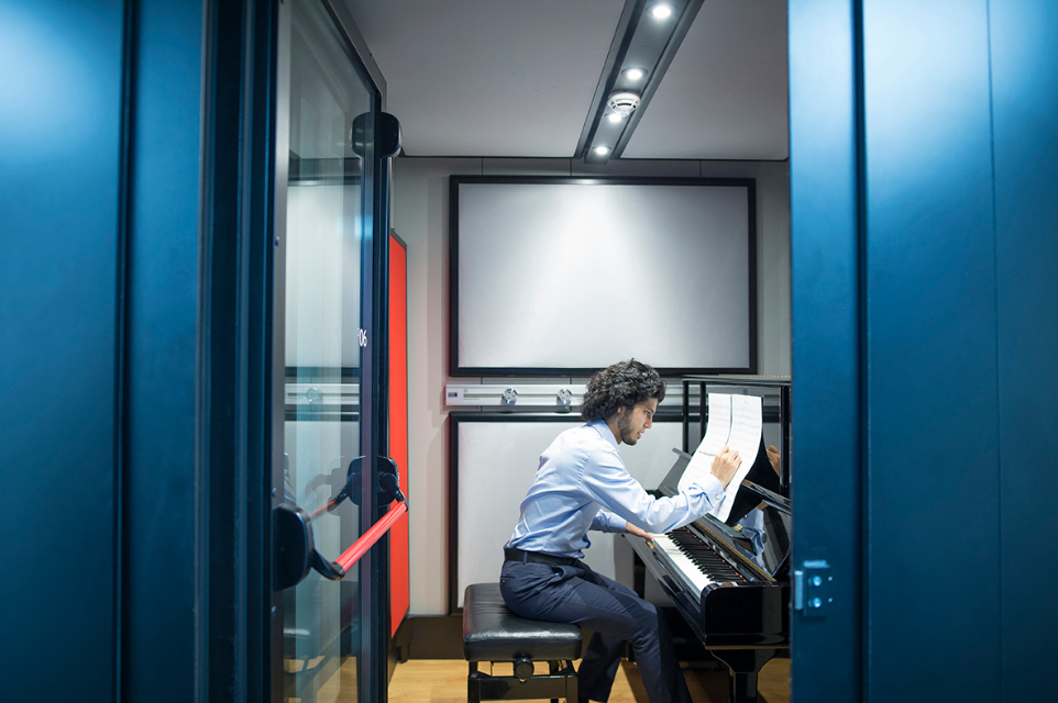 A male student practising on the piano, in a practise pod.